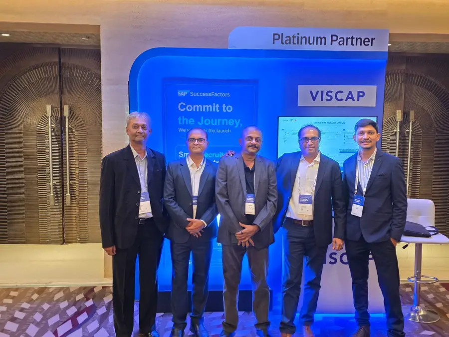 Five members of the VISCAP team at the VISCAP stand, under the Platinum Partner sign.