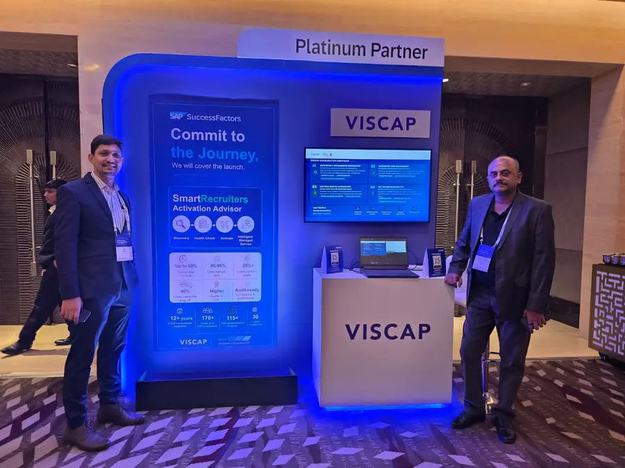 Two members of the VISCAP team at the stand, with VISCAP&rsquo;s SAP accelerator portfolio on the screen behind them.