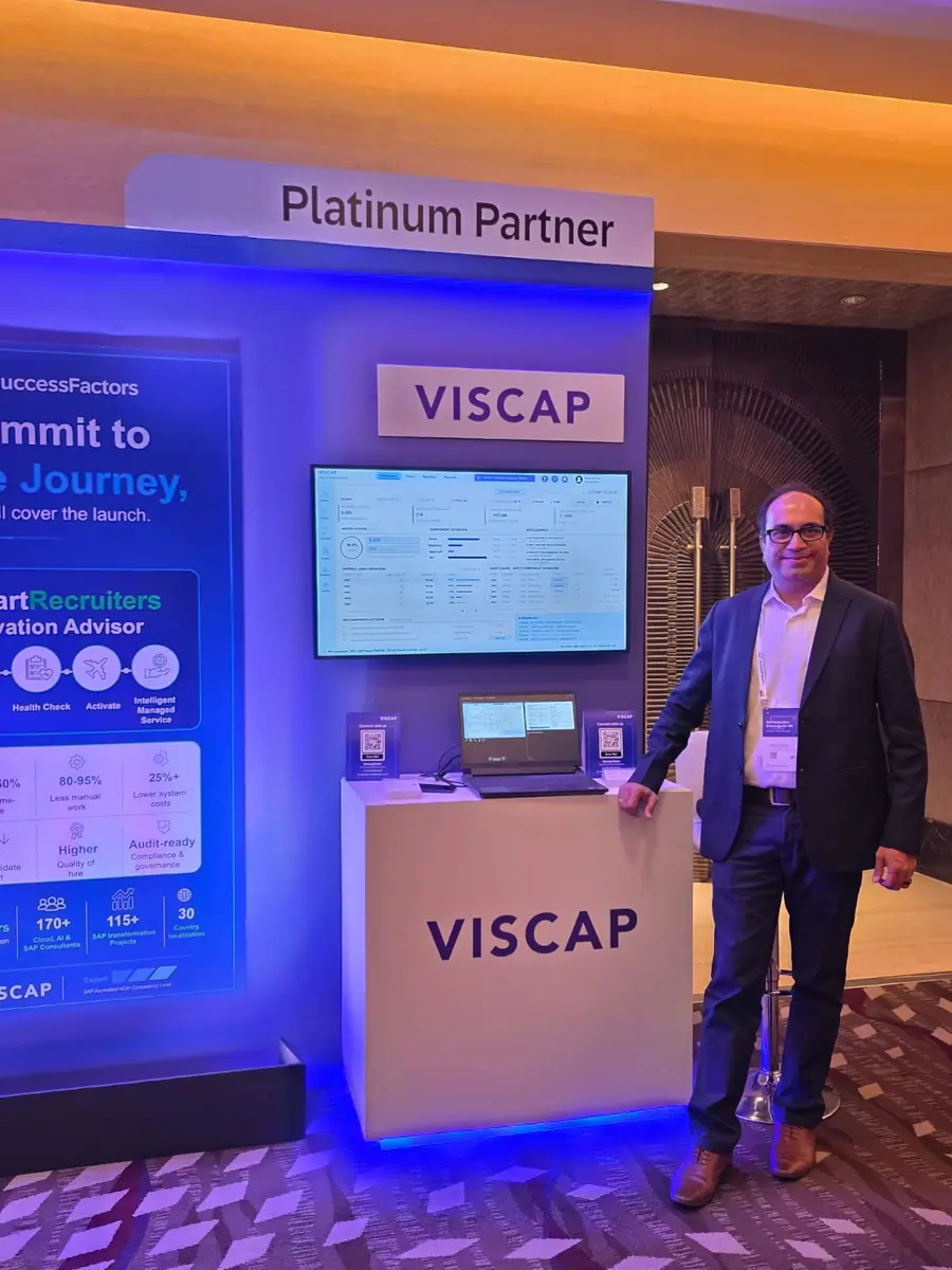 A member of the VISCAP team at the stand, with a VISCAP payroll control dashboard on the screen alongside.