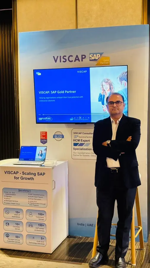 Darshan Suthar, de VISCAP, sur le stand, à côté du panneau de la spécialisation SuccessFactors HCM Expert.